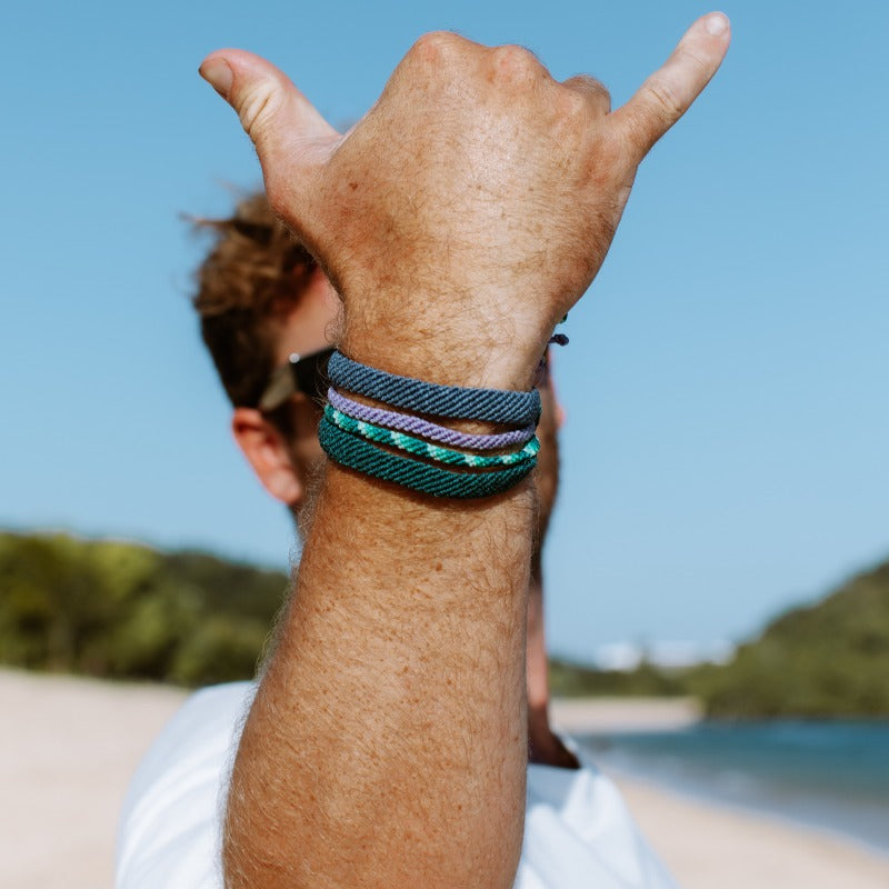 surf bracelets on mens hand doing shaka on beach