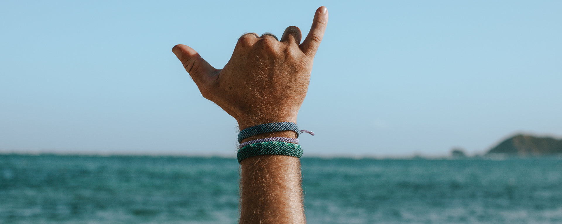 waxed waterproof bracelets on mens hand making shaka sign over the ocean